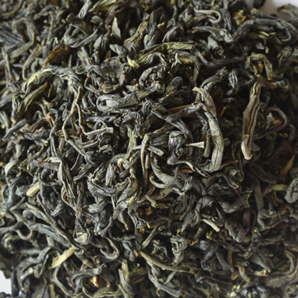 A close-up of loose leaf Spring Green tea, showcasing twisted, dark green leaves with hints of lighter green. The leaves appear slightly curled and have a rich, earthy texture.