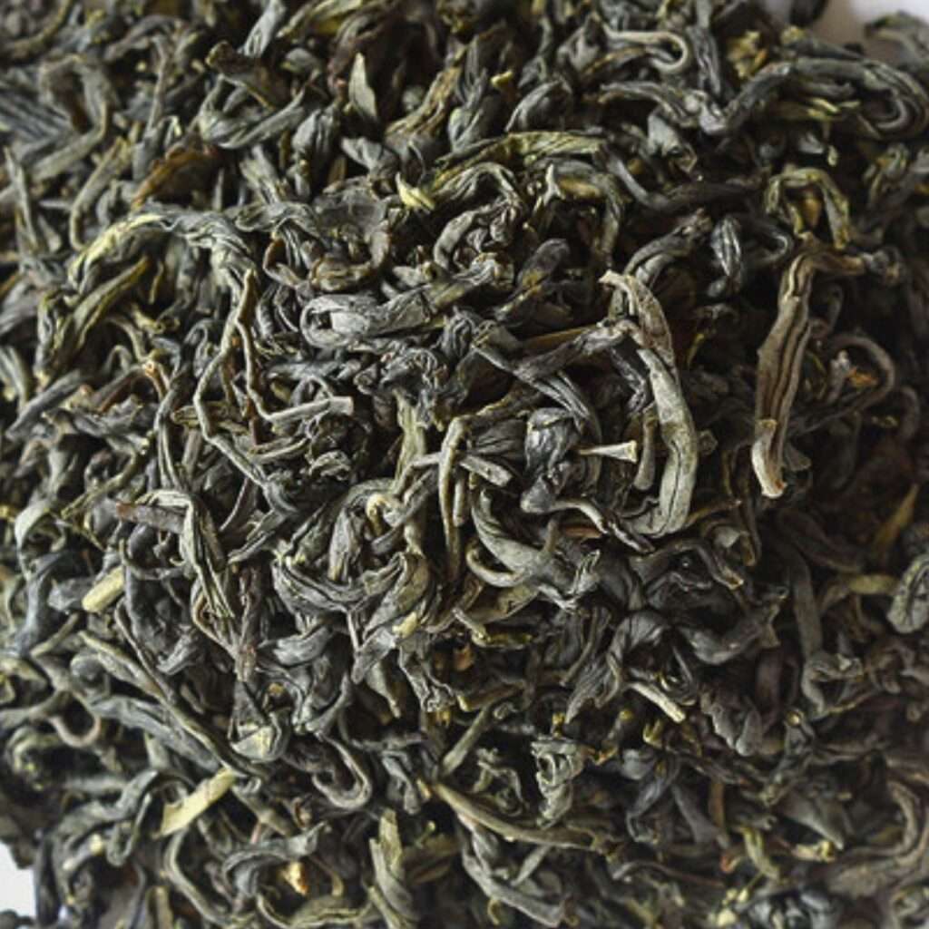 A close-up of loose leaf Spring Green tea, showcasing twisted, dark green leaves with hints of lighter green. The leaves appear slightly curled and have a rich, earthy texture.
