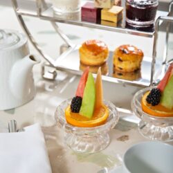 Tiered stand of afternoon tea with scones, jam, clotted cream, and fresh fruit
