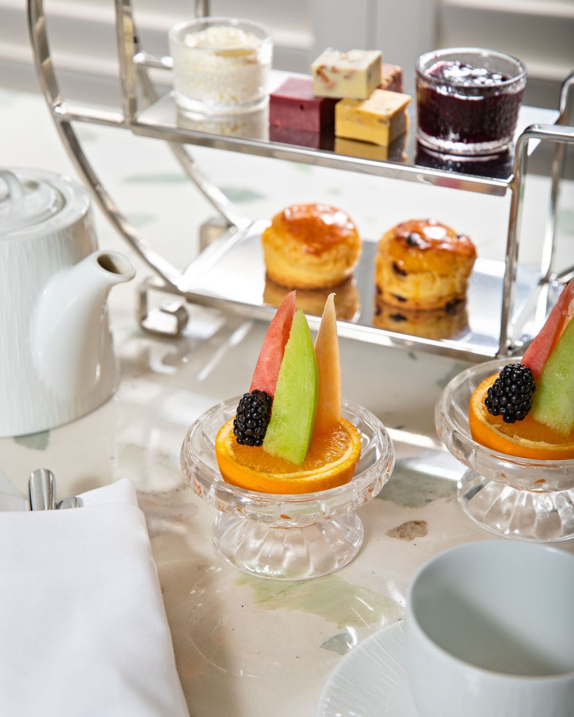 Tiered stand of afternoon tea with scones, jam, clotted cream, and fresh fruit