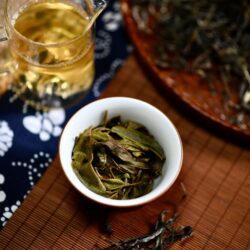 Lightly oxidized Baozhong oolong tea leaves beside a cup of pale golden brewed tea