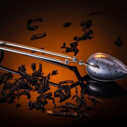 Broken black tea leaves scattered around a stainless steel tea infuser