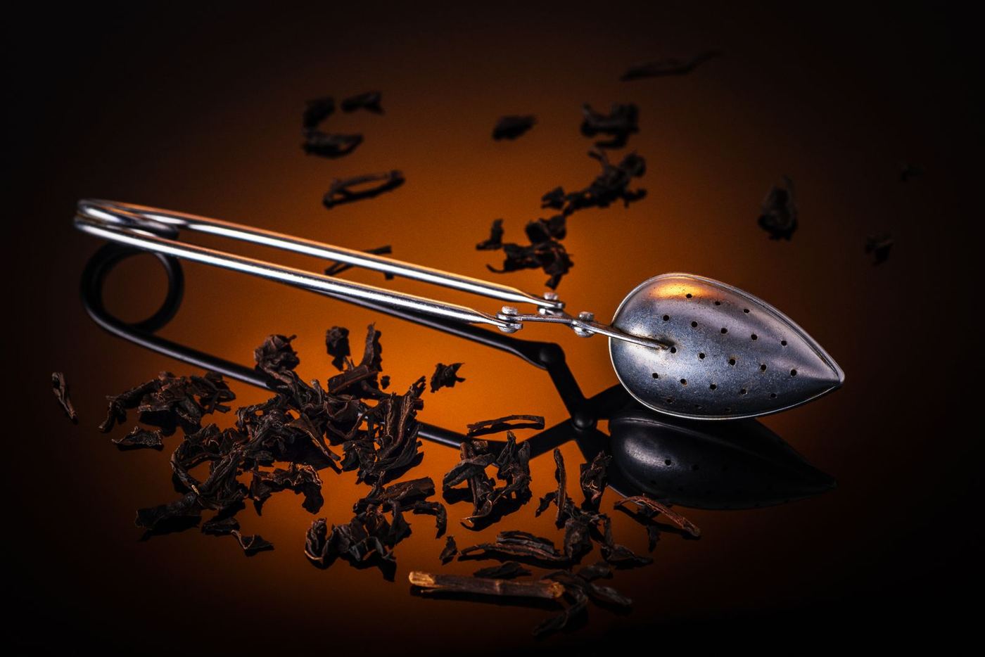 Broken black tea leaves scattered around a stainless steel tea infuser