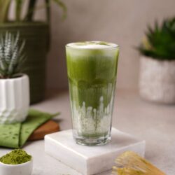 Iced matcha latte in a glass with matcha powder and bamboo whisk nearby