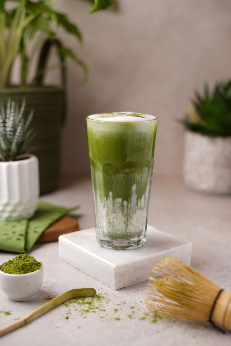 Iced matcha latte in a glass with matcha powder and bamboo whisk nearby