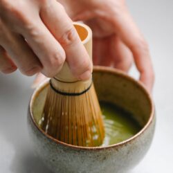 Hands whisking bright green ceremonial matcha with a bamboo chasen in a rustic bowl