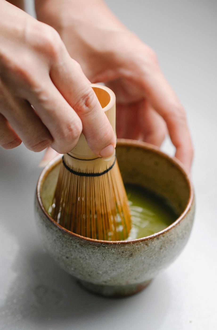 Hands whisking bright green ceremonial matcha with a bamboo chasen in a rustic bowl