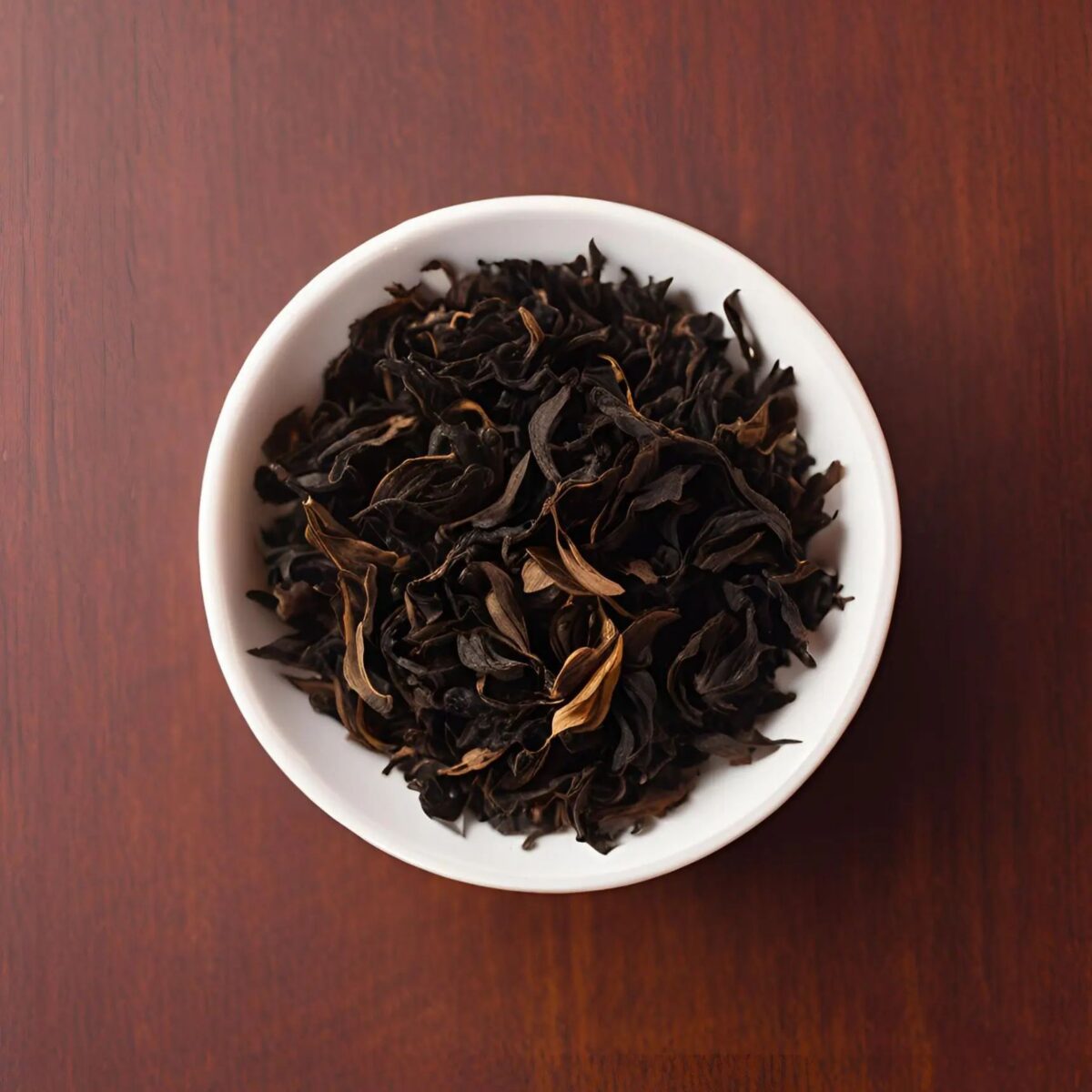 Dark, curled, fully oxidized black tea leaves in a white bowl