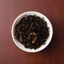 Dark, curled, fully oxidized black tea leaves in a white bowl