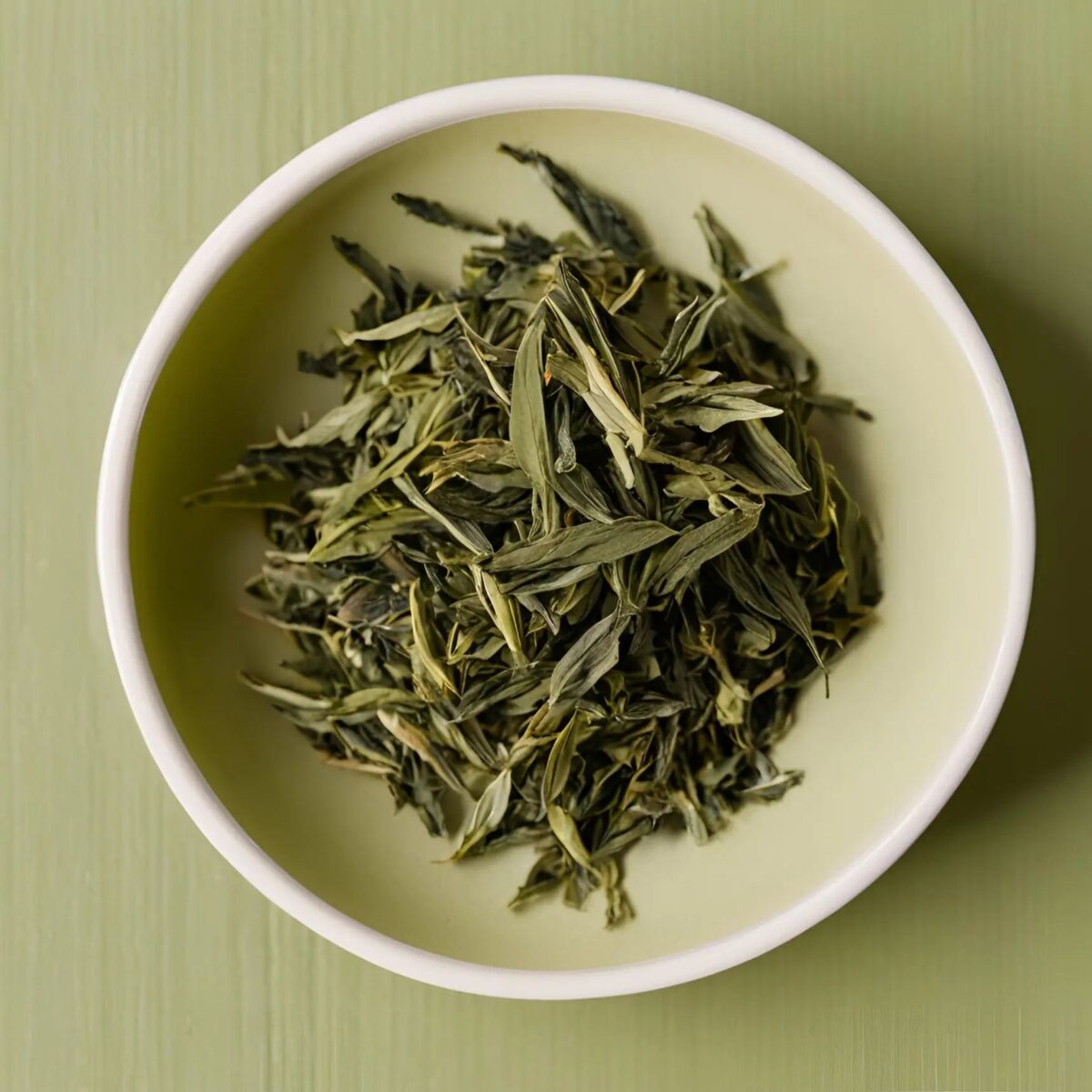 Green tea leaves, minimally processed, in a white bowl