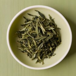 Green tea leaves, minimally processed, in a white bowl