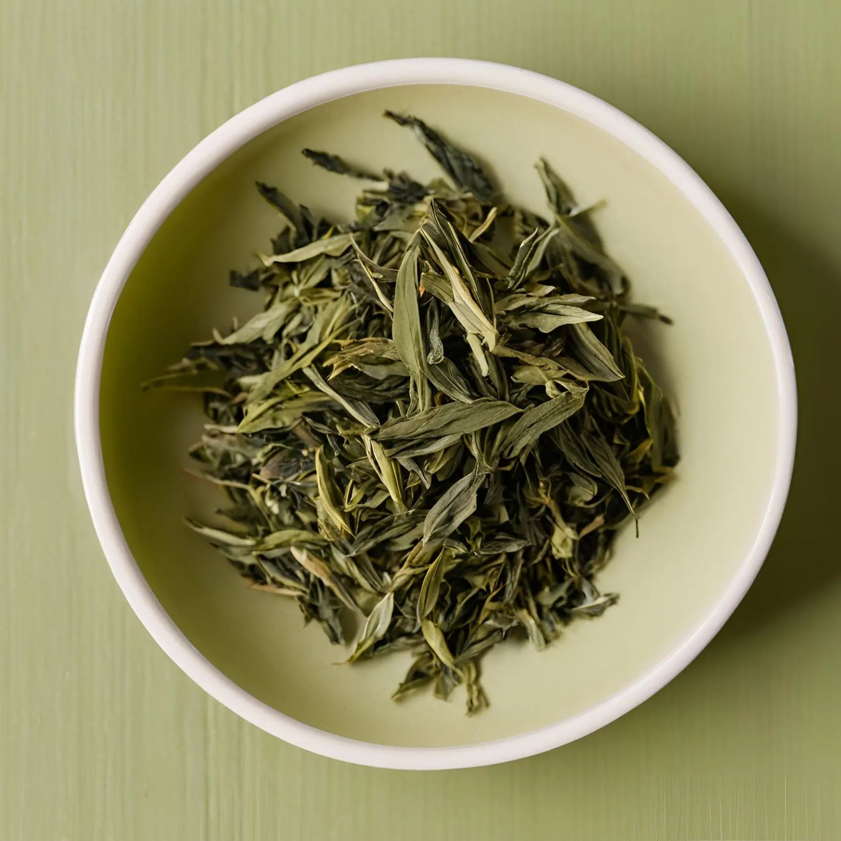 Green tea leaves, minimally processed, in a white bowl