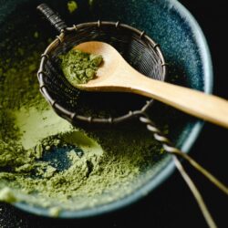 Vivid green matcha powder in a sifter with a wooden spoon
