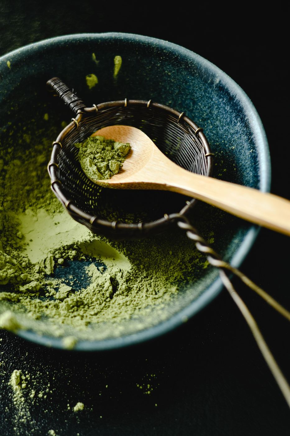 Vivid green matcha powder in a sifter with a wooden spoon