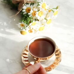 Cup of tea beside a bundle of fresh white chamomile flowers
