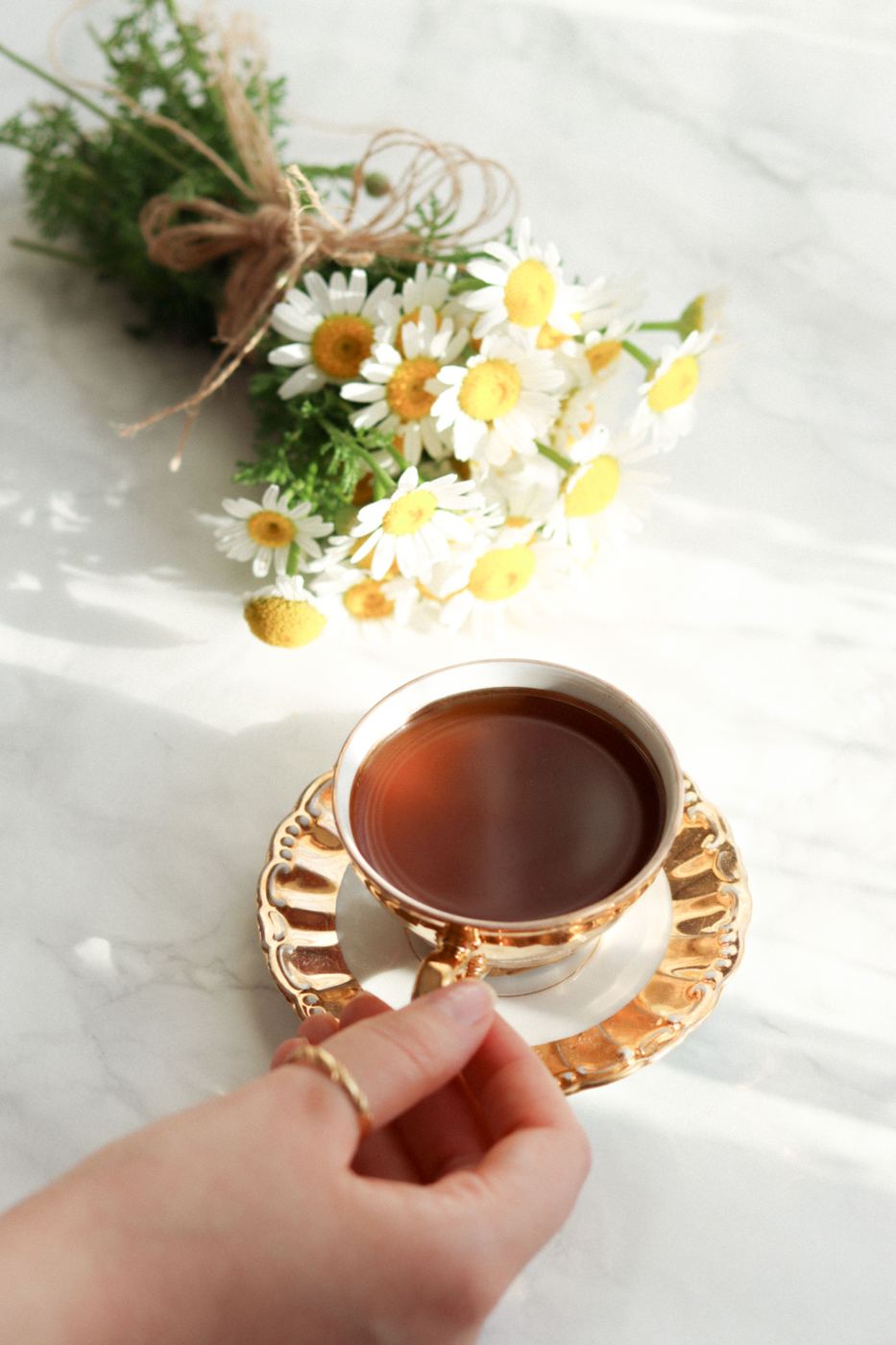 Cup of tea beside a bundle of fresh white chamomile flowers