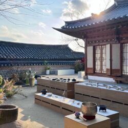 A traditional Korean hanok courtyard with tiled roofs, set up with wooden platforms holding tea implements for a tea gathering