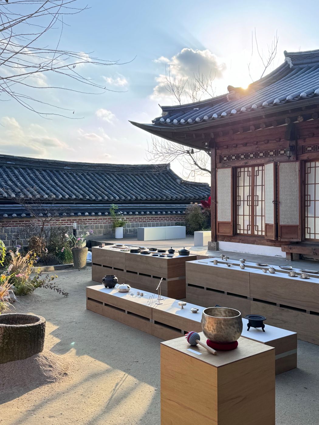 A traditional Korean hanok courtyard with tiled roofs, set up with wooden platforms holding tea implements for a tea gathering