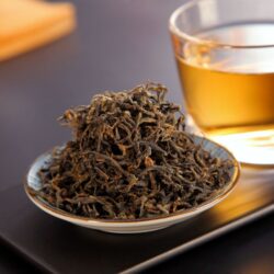 Whole-leaf black tea with abundant golden tips beside a cup of brewed amber tea, representing the finest tippy golden flowery orange pekoe (FTGFOP) grade