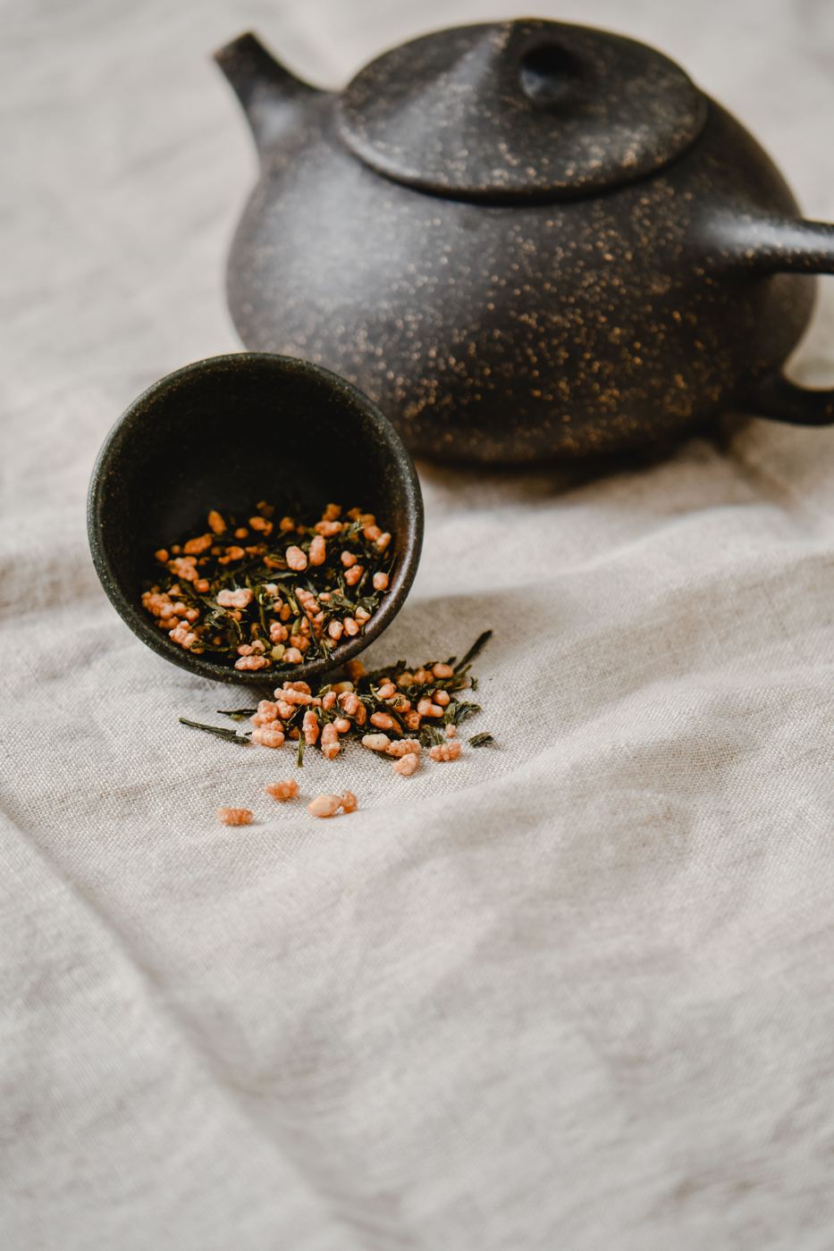 Genmaicha loose leaf tea with roasted brown rice grains beside a dark teapot