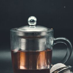 Loose black tea leaves steeping directly in hot water in a glass mug with a built-in metal infuser basket