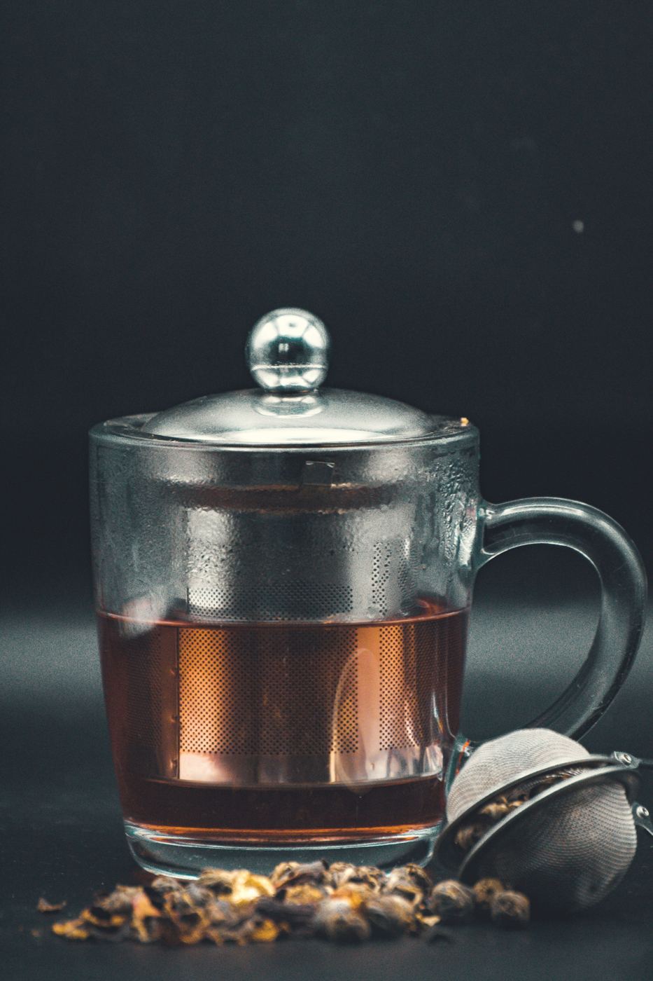 Loose black tea leaves steeping directly in hot water in a glass mug with a built-in metal infuser basket