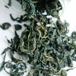 Dark green, tightly rolled whole-leaf Gyokuro tea spilling from a glass bowl