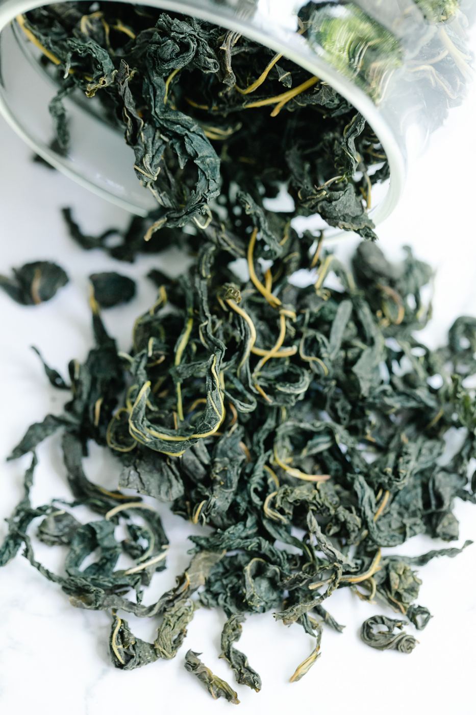 Dark green, tightly rolled whole-leaf Gyokuro tea spilling from a glass bowl