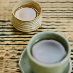 Two ceramic cups of reddish-brown roasted Hojicha tea on a woven mat