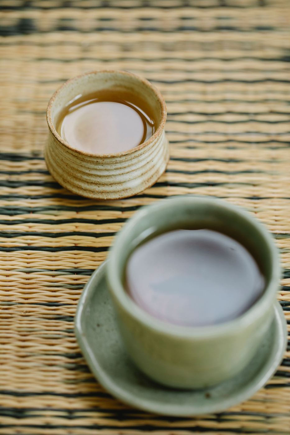 Two ceramic cups of reddish-brown roasted Hojicha tea on a woven mat