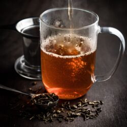 Hot water being poured into a glass of steeping loose leaf tea