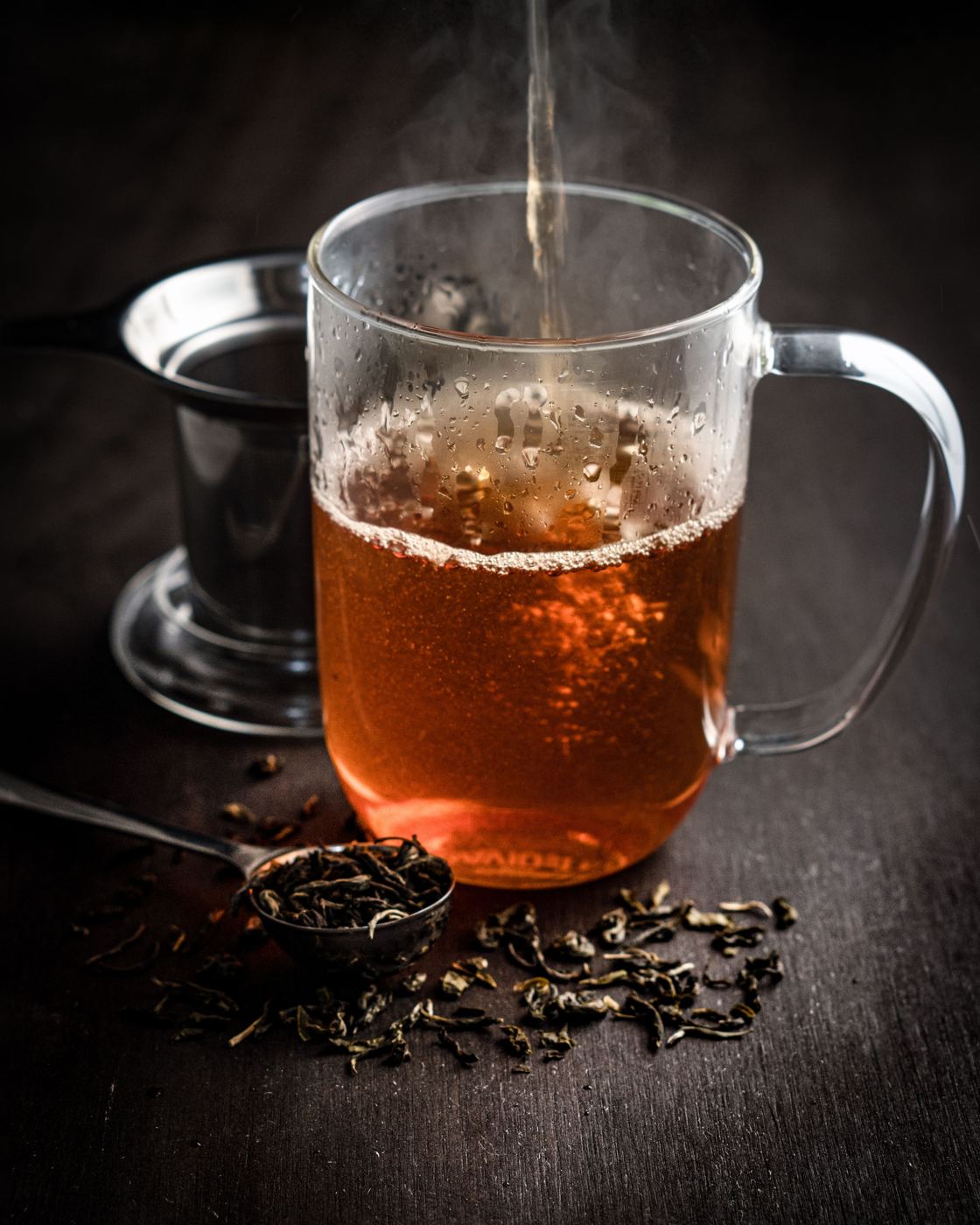 Hot water being poured into a glass of steeping loose leaf tea