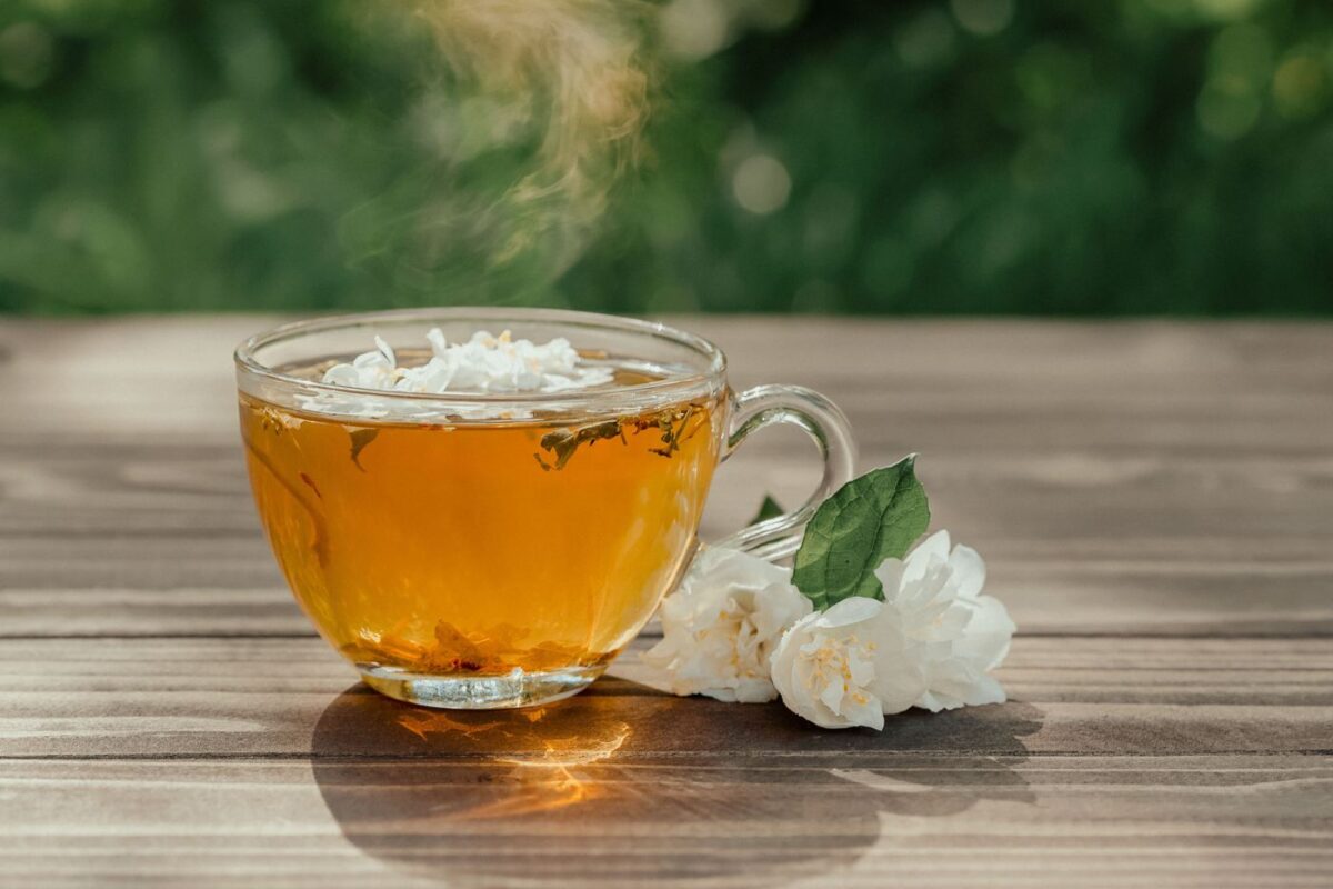 Glass cup of golden jasmine tea beside fresh white jasmine blossoms outdoors