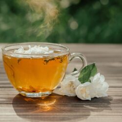 Glass cup of golden jasmine tea beside fresh white jasmine blossoms outdoors