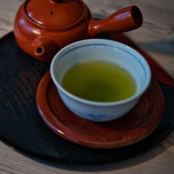 A red clay Japanese kyusu teapot with side handle beside a cup of green tea