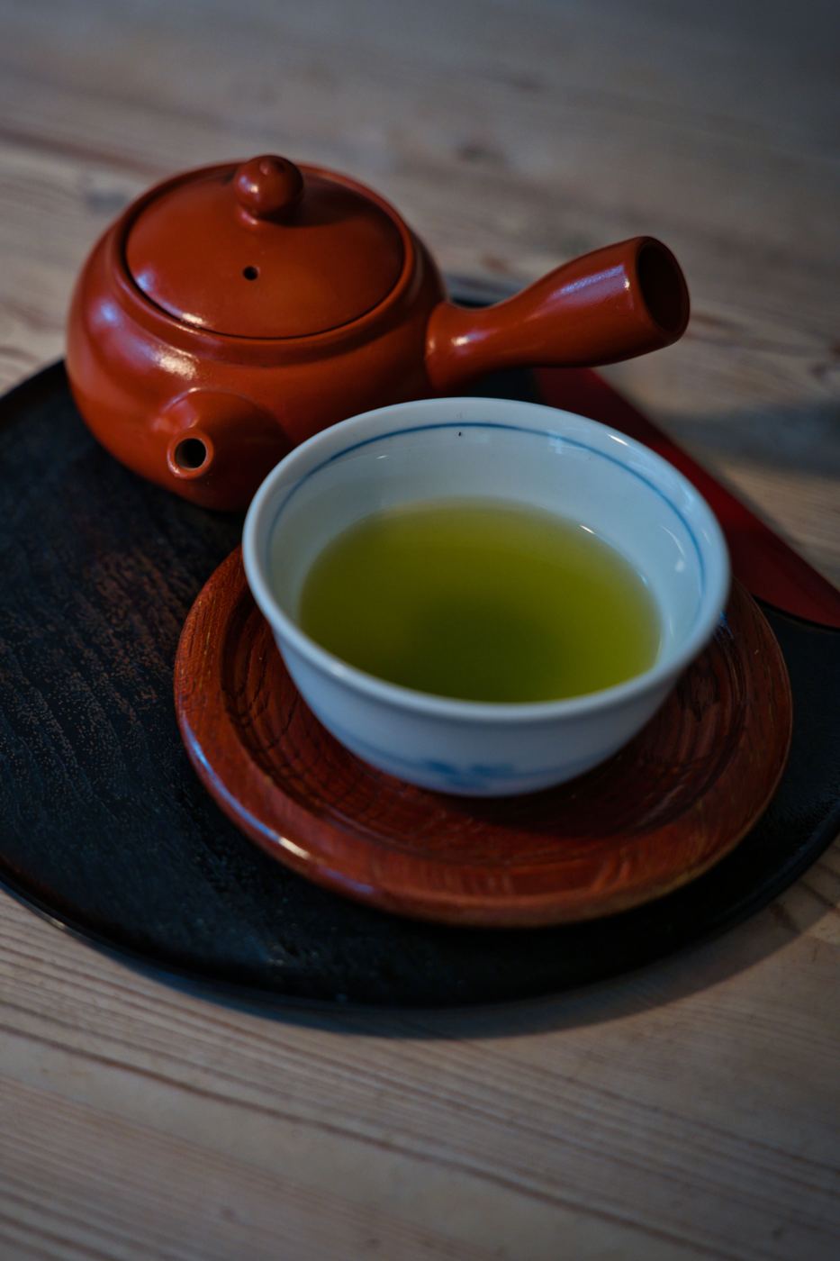 A red clay Japanese kyusu teapot with side handle beside a cup of green tea