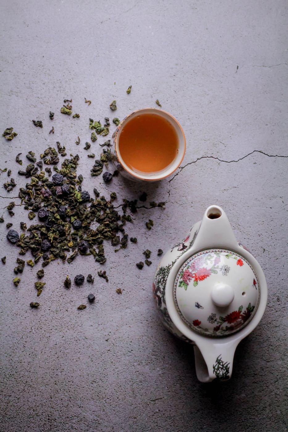 Rolled oolong tea leaves scattered beside a cup of golden brewed tea and a decorative teapot