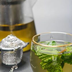 Fresh mint leaves steeping in a glass teacup beside a glass teapot