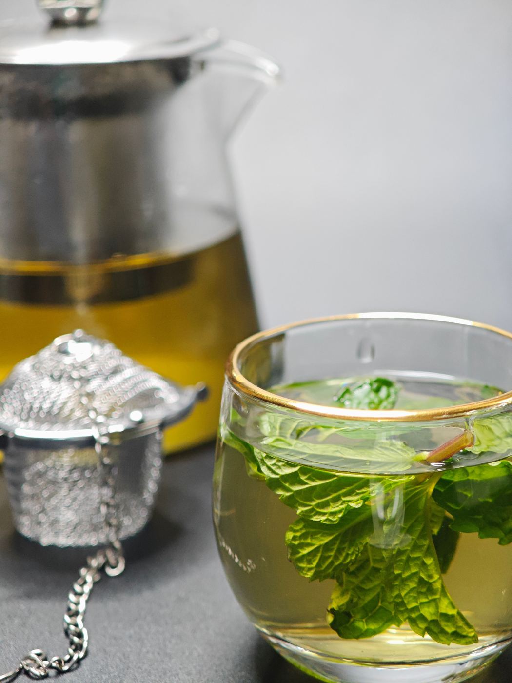 Fresh mint leaves steeping in a glass teacup beside a glass teapot