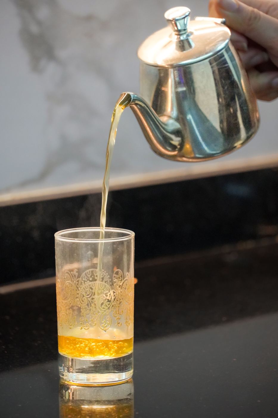 Mint tea poured from a height out of a silver teapot into an engraved Moroccan glass