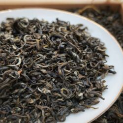 Close-up of dark, curled, fully oxidized black tea leaves on a white plate