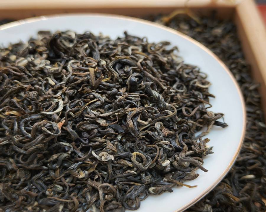 Close-up of dark, curled, fully oxidized black tea leaves on a white plate