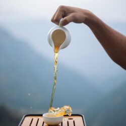 Tea poured from a small pot into a cup, with misty Himalayan mountains in the background