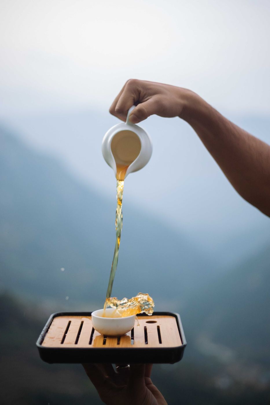 Tea poured from a small pot into a cup, with misty Himalayan mountains in the background