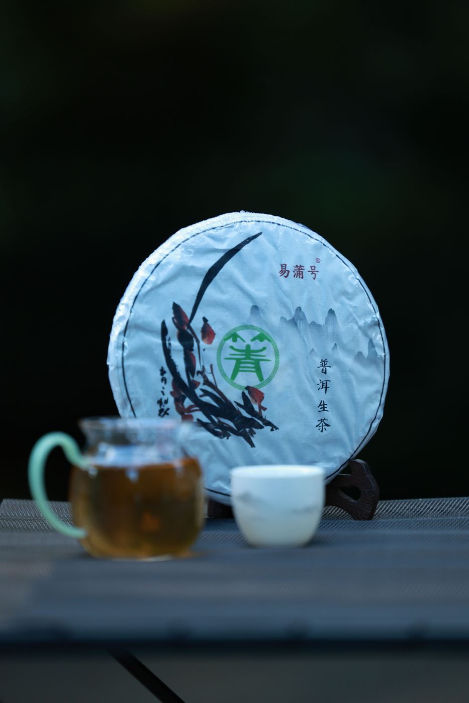 Compressed Chinese pu-erh tea cake labeled sheng cha beside a cup of brewed dark tea