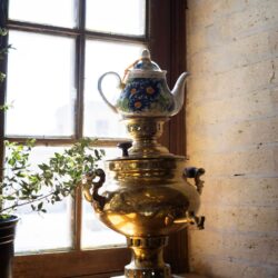 A brass Russian samovar with a small teapot on top, sitting on a sunlit windowsill