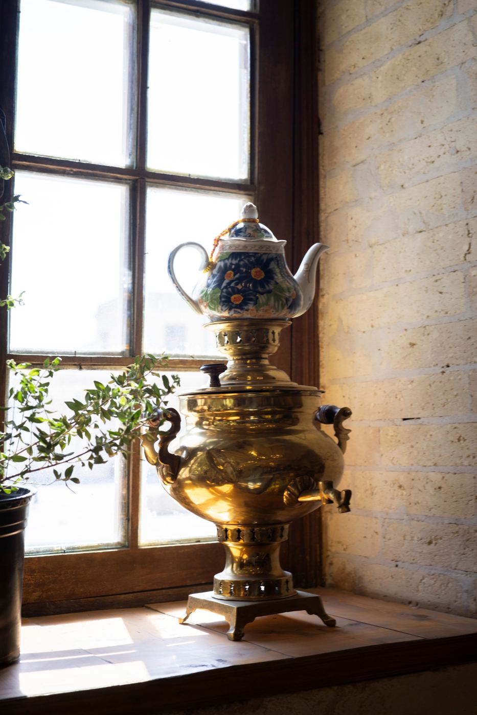 A brass Russian samovar with a small teapot on top, sitting on a sunlit windowsill