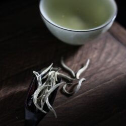 White tea leaves and buds on a wooden tray beside a cup of brewed tea