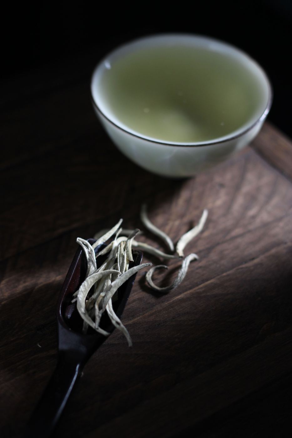 White tea leaves and buds on a wooden tray beside a cup of brewed tea
