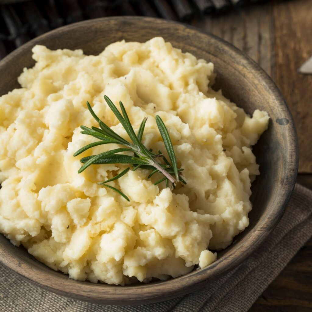 A bowl of smooth, creamy Rosemary Lemonade Mashed Potatoes, topped with a sprig of fresh rosemary, showcasing the herbaceous twist brought by Rosemary Lemonade tea.